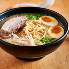 a bowl of ramen with meat, noodles and boiled egg on the side sitting on a wooden table