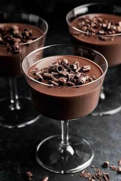 three glasses filled with chocolate pudding on top of a black table next to some nuts