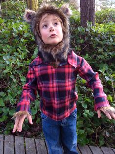 a young boy wearing a furry hat and plaid shirt with his hands out in the air