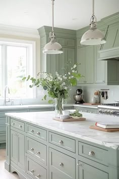 a kitchen with green cabinets and marble counter tops, white flowers in a vase on the island