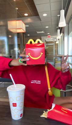 a woman sitting at a table with a mcdonald's bag on her head and a drink in front of her face