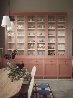 a dining room table and chairs with pink china cabinet in the backround area