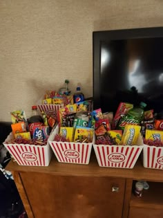 three buckets filled with candy sitting on top of a wooden dresser next to a tv