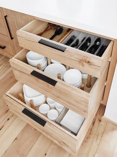 an open drawer with dishes and utensils in it on the floor next to a counter