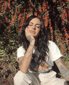 a woman sitting on the ground with her hands to her face and flowers in the background