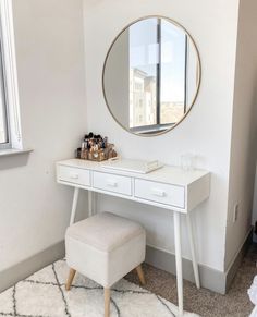 a white dressing table with a mirror and stool in a small room next to a window