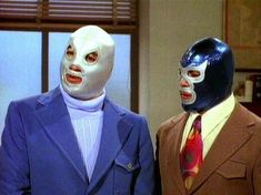 two men in suits and masks stand next to each other, one wearing a suit