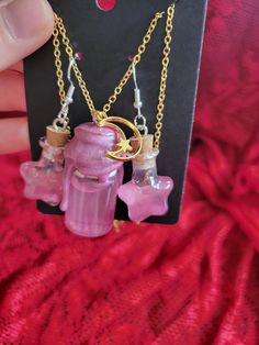 a pink necklace with two small glass bottles hanging from it's sides on a gold chain