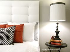 a bed with white headboard and pillows next to a lamp on a night stand