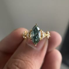 a person holding a ring with a green stone in it's middle and two white diamonds on the side