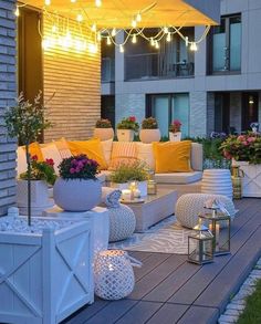 an outdoor living area with white furniture and yellow pillows on the couches, surrounded by potted plants