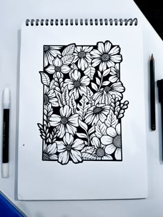 a black and white drawing of flowers in a square frame on top of a notebook