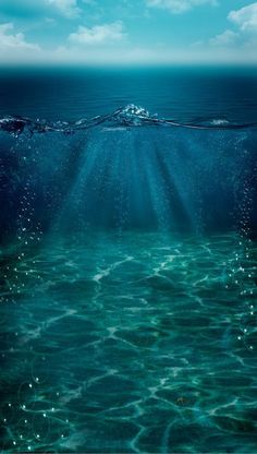 an underwater view of the ocean with blue sky and sunbeams in the background