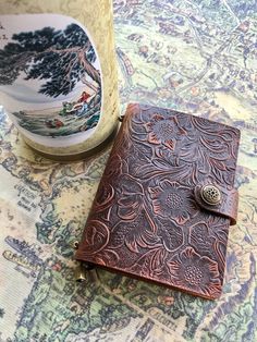 a brown leather journal sitting on top of a table next to a vase and cup