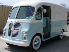 an old blue and white truck parked in a parking lot with its door open to the side