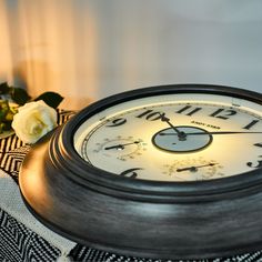 a black and white clock sitting on top of a table next to a vase with flowers