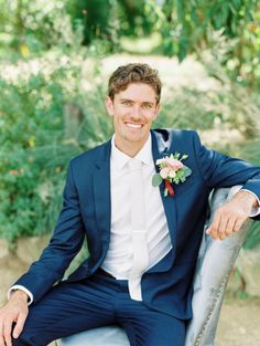 a man in a blue suit and white shirt sitting on a chair smiling at the camera