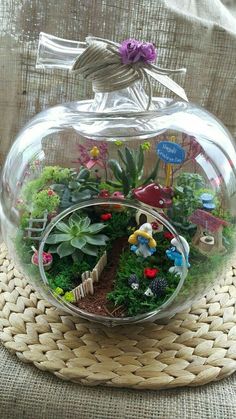 a glass bowl filled with lots of plants and small animals on top of a table