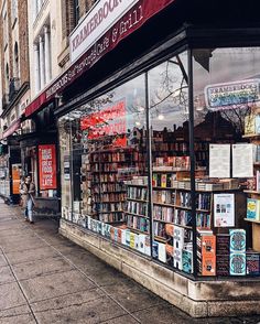 a book store on the side of a street with people walking past it and there are many books in the window