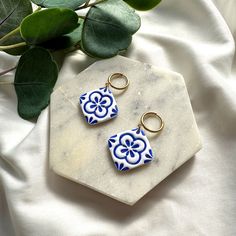 two blue and white tile earrings sitting on top of a marble slab next to a plant