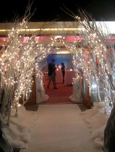 an archway decorated with white lights and trees in the middle of snow covered walkways