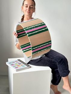 a woman sitting on top of a white table holding up a large piece of cardboard