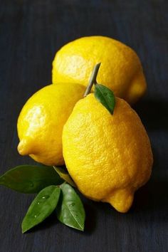 three lemons with green leaves on a table