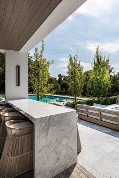 an outdoor kitchen with marble counter tops and bar stools next to the swimming pool