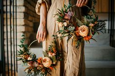 a woman holding two wreaths with flowers and greenery hanging from the front of her body