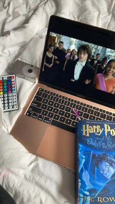 an open laptop computer sitting on top of a bed next to a book and remote control