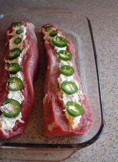 two raw meats with cheese and green peppers on them sitting in a glass dish