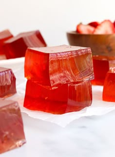 several pieces of red gummy candy sitting on top of white paper next to strawberries