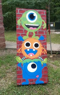 two monsters painted on the side of a red brick wall in front of trees and grass