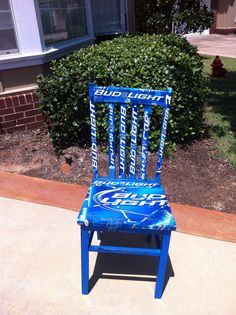 a blue chair sitting on top of a sidewalk next to a bush and building in the background