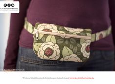 a woman is wearing a belt bag with flowers on it and has her hands in the pocket