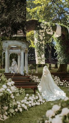 a woman in a wedding dress is sitting on a park bench with flowers all around her