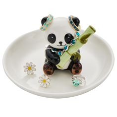 a small panda bear figurine sitting on a plate holding a piece of jewelry