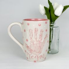 there is a coffee cup with a handprint on it and flowers in the vase