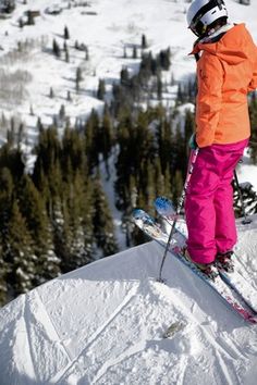 a person riding skis on top of a snow covered slope with trees in the background