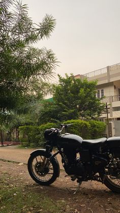 a black motorcycle parked on the side of a road next to a tree and building