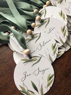 several tags with green leaves on them are sitting on a table next to some ribbons