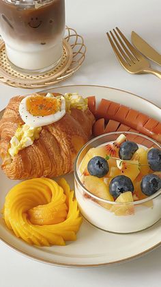 a white plate topped with croissants and fruit next to a cup of coffee