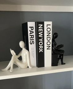 a couple of books sitting on top of a white shelf next to a black and white figurine