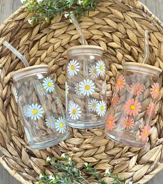 three glass tumblers with painted daisies on them sitting in a basket next to flowers