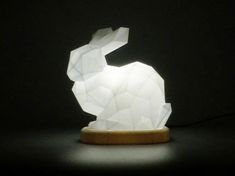 an origami rabbit lamp sitting on top of a wooden base in the dark