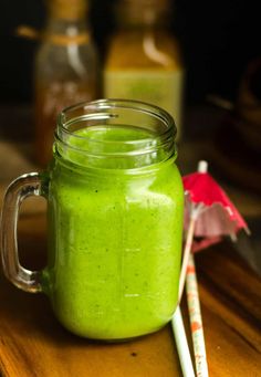 a green smoothie in a mason jar with two straws next to it on a wooden table