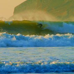 a man riding a wave on top of a surfboard in the ocean next to a mountain