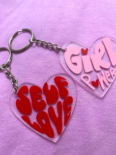 two heart shaped key chains with the words girl power written on them, one in red and one in pink