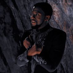 a man standing in front of a rock wall with his hands folded up and looking off to the side