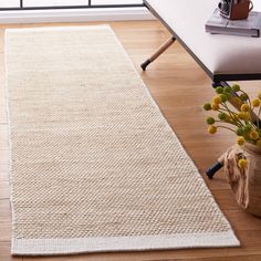 a white rug on top of a wooden floor next to a couch and table with flowers